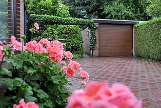 Garage mit grüner Hecke und Rosa Blumenbeet