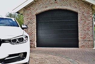 Backsteingarage mit schwarzem Tor und weißem Auto