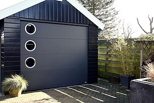 Schwarze Garage mit grauem Tor mit runden Fenstern